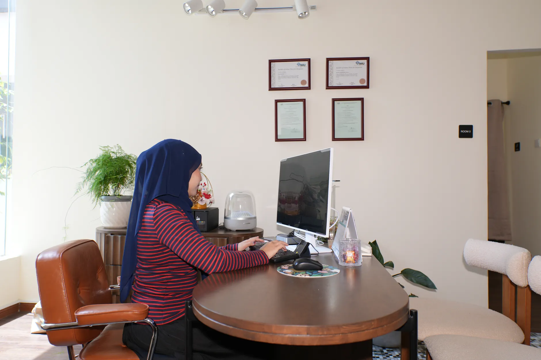 The bright, plant-filled reception area of the Kind Chiropractic clinic in Bangsar, with a team member working at the front desk