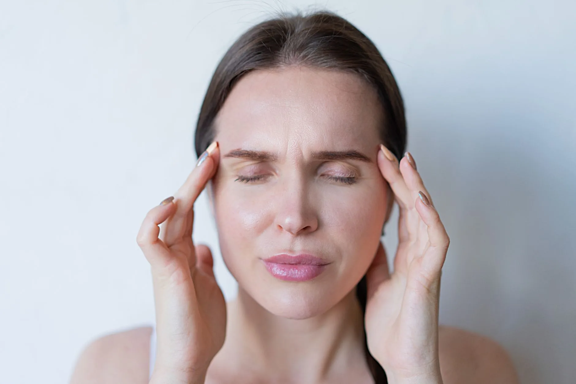 Woman holding her temples with her eyes closed, showing the strain of a migraine or tension headache