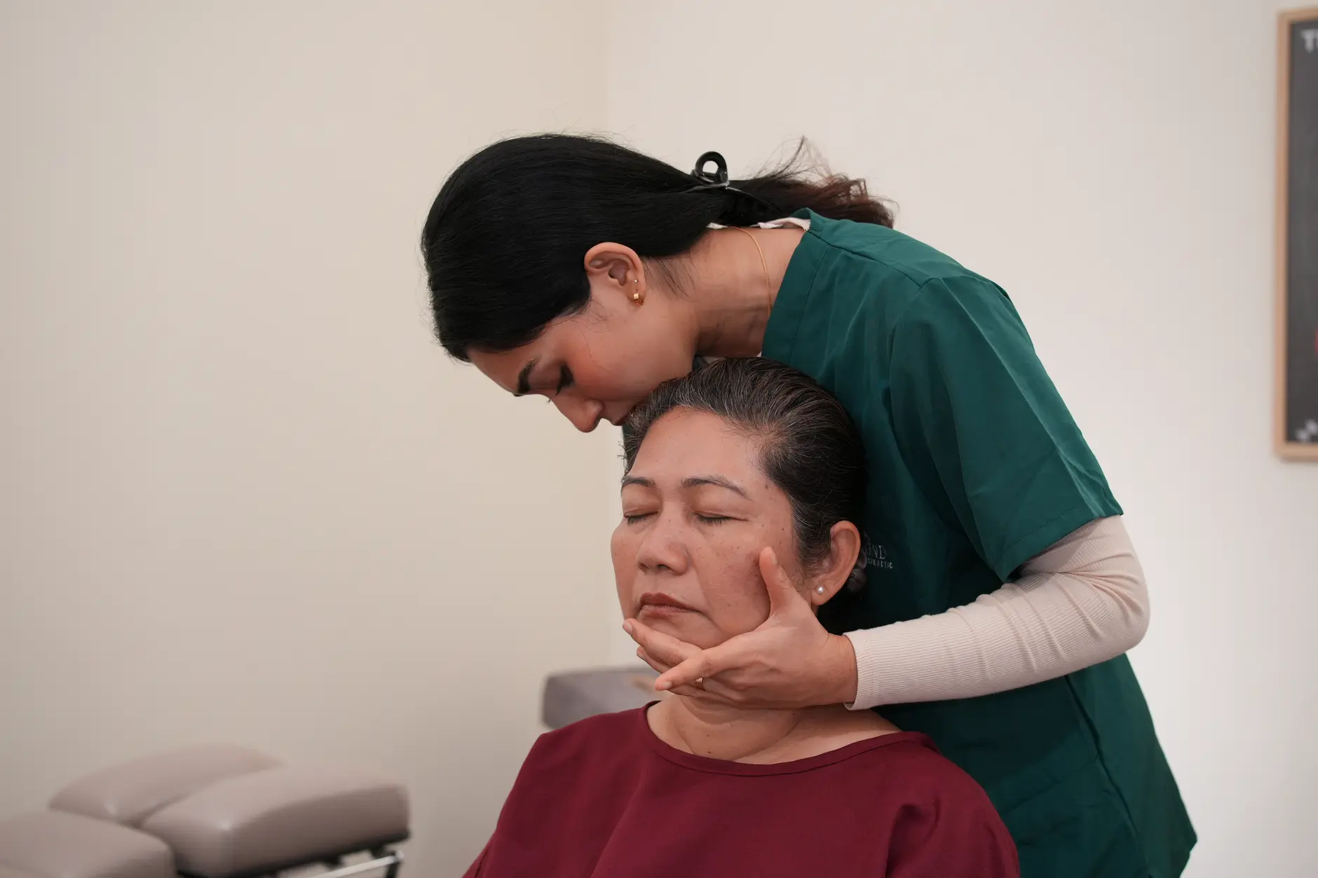 A chiropractor providing gentle hands-on cervical care to a seated older woman at Kind Chiropractic, with careful attention to upper neck positioning