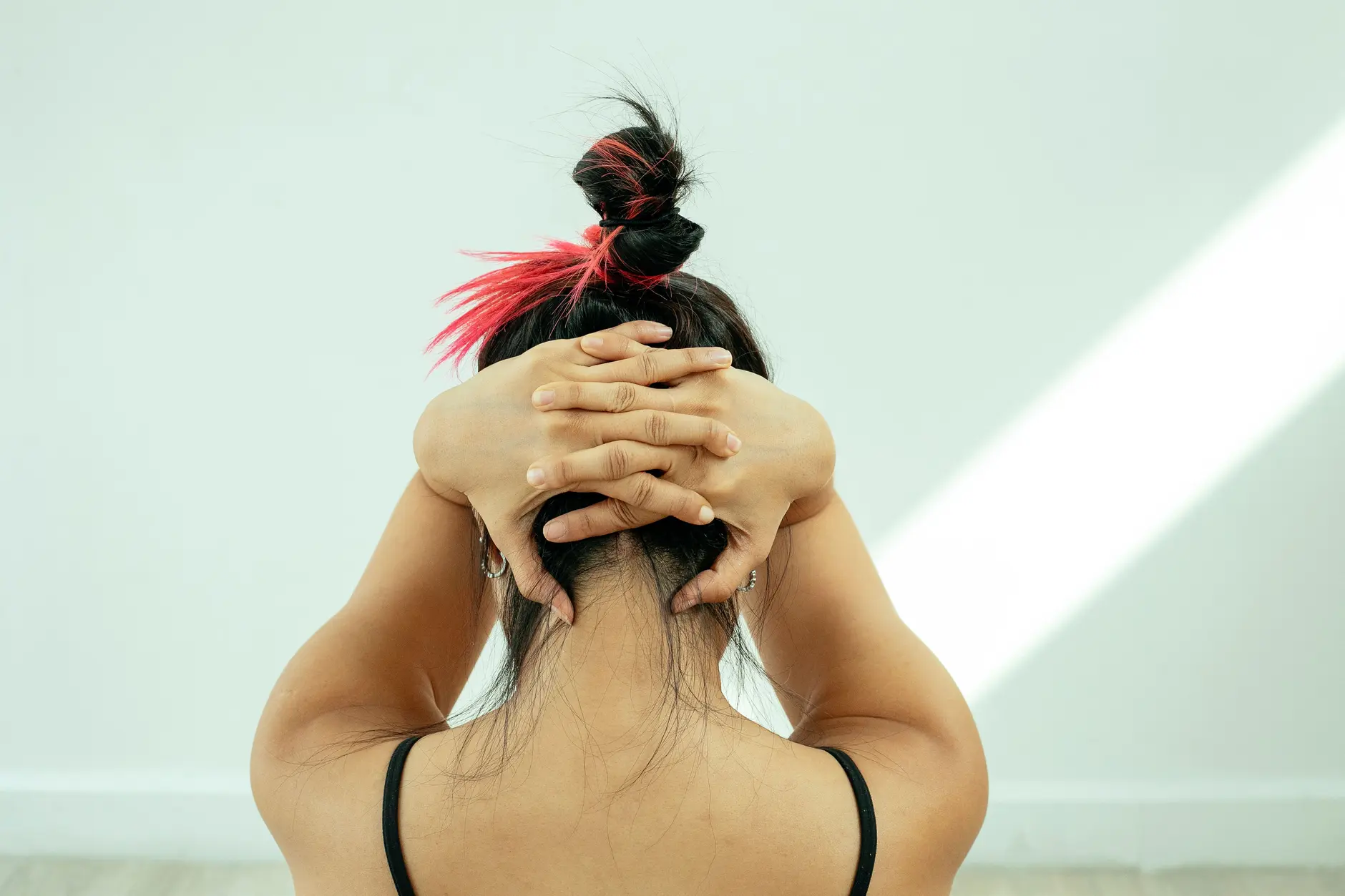 A person viewed from the back performing a neck and upper-back stretch, arms raised and elbows out in a corrective posture exercise