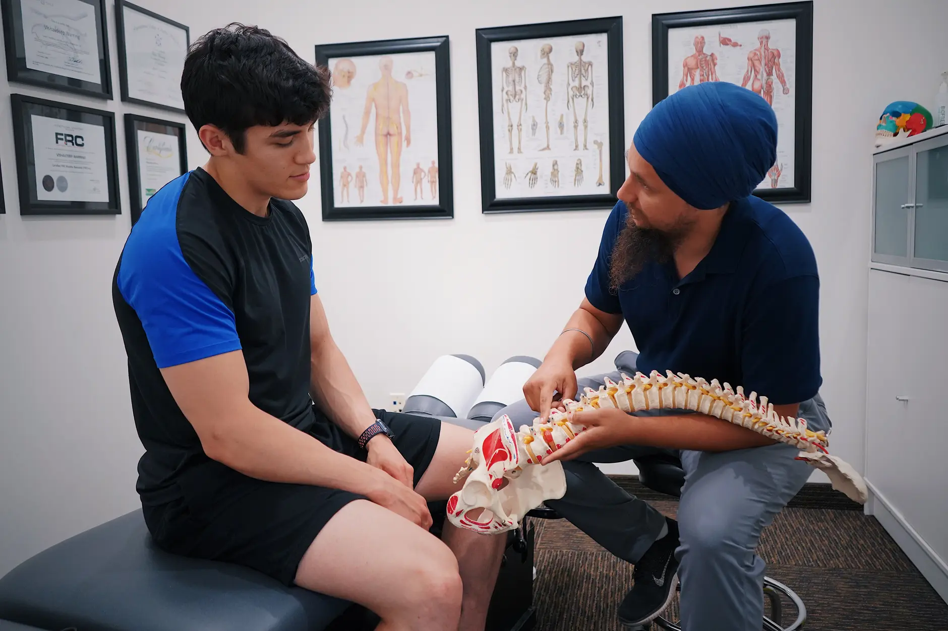 A practitioner explaining a spine model to a seated patient, illustrating how careful and specific chiropractic adjustments work