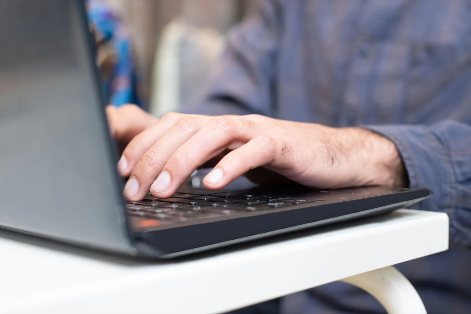 Close-up of a person typing at a laptop with bent wrists resting on the desk edge, a posture that narrows the carpal tunnel