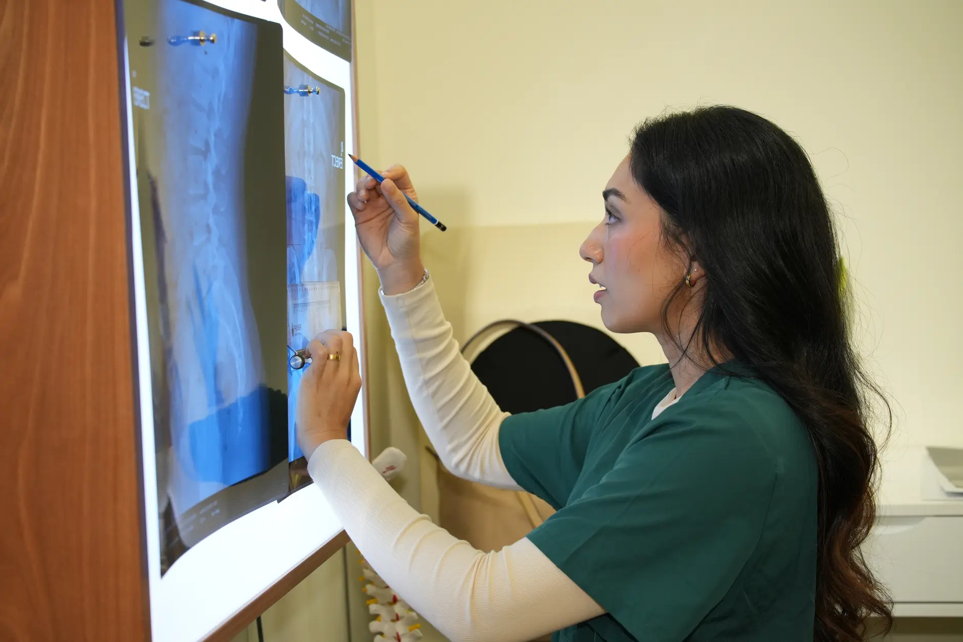 A clinician analysing spinal X-ray films on a lightbox to assess cervical and thoracic alignment in a shoulder pain case
