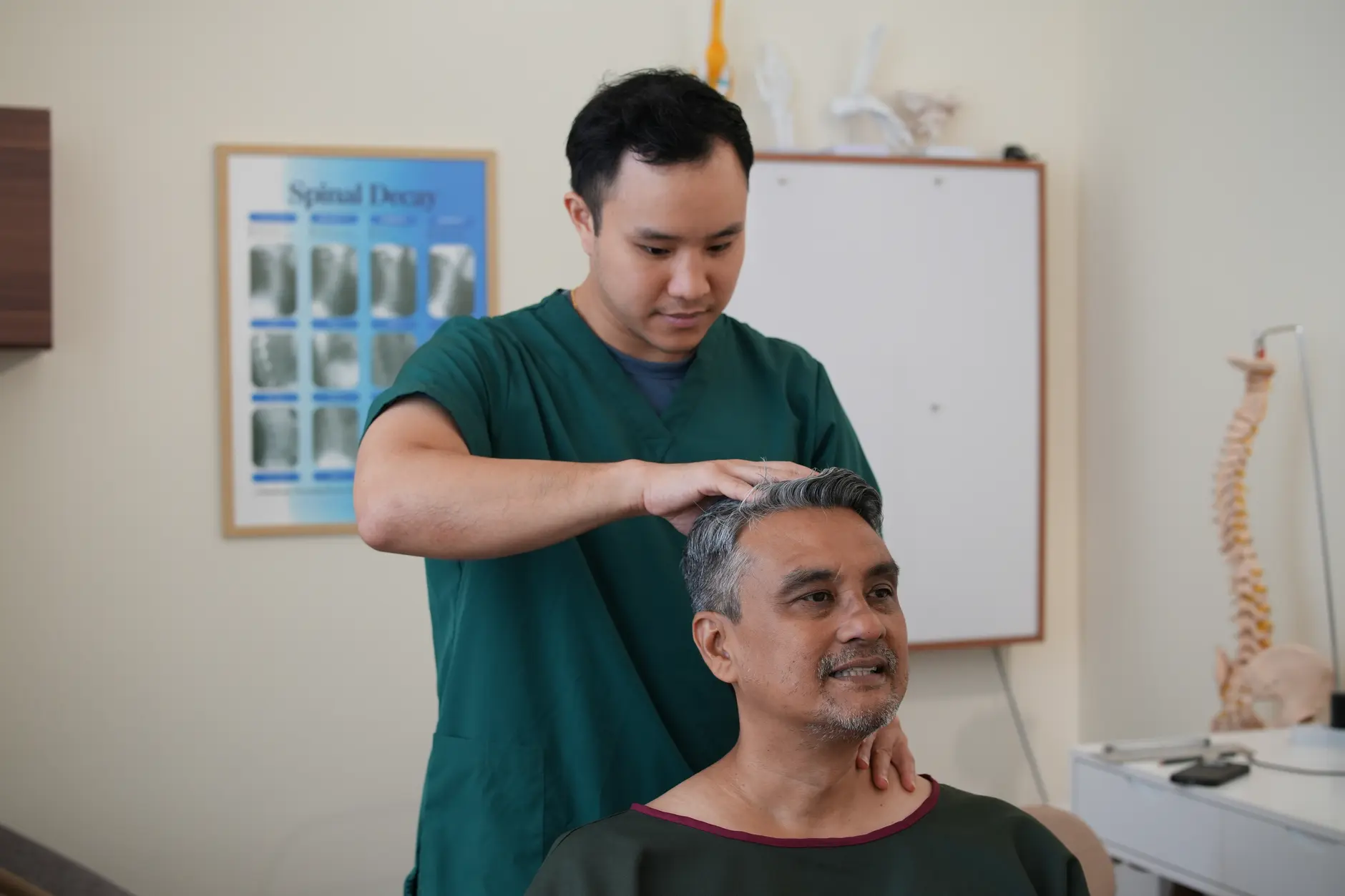 A chiropractor with hands on a seated man's neck and head, performing cervical assessment for referred shoulder pain