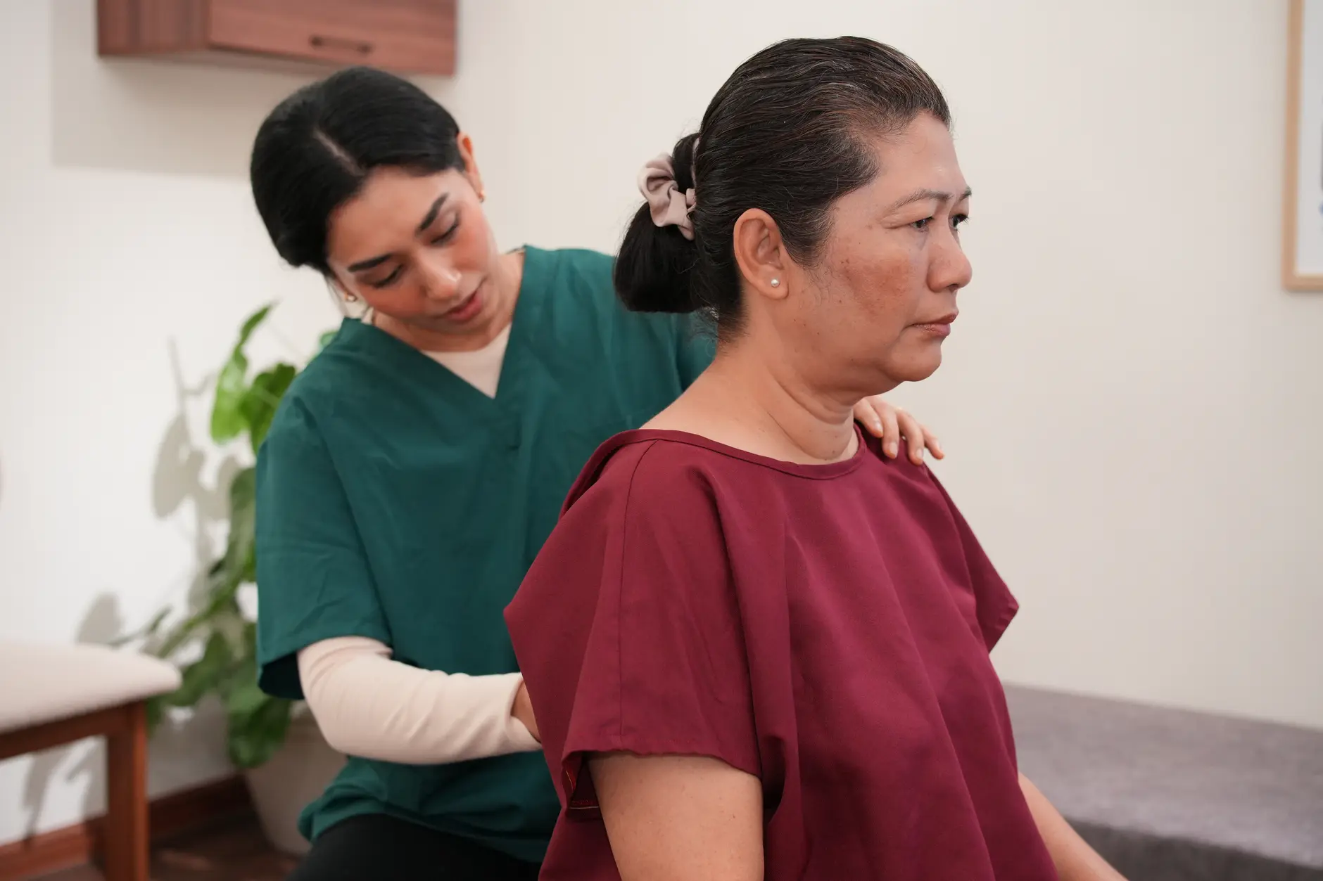 A chiropractor treating a seated older woman's shoulder and upper back from behind, applying hands-on shoulder care