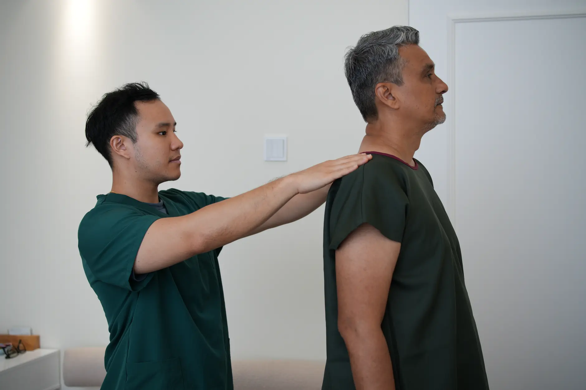 Chiropractor assessing a standing male patient's shoulder and upper back posture from the side at Kind Chiropractic Kuala Lumpur