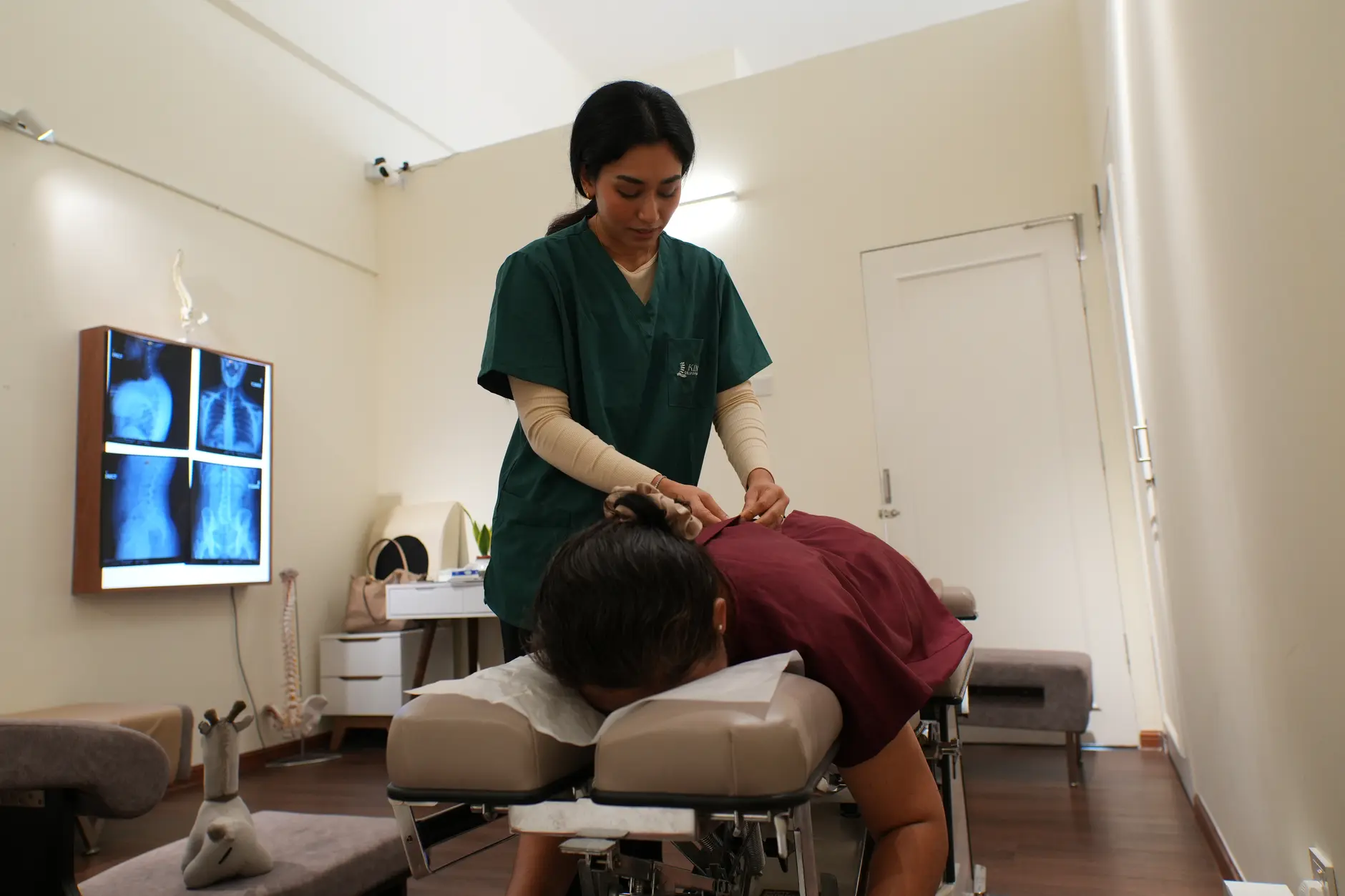 Chiropractor treating a patient with a slipped disc on an adjustment table at Kind Chiropractic KL, with spinal X-rays displayed nearby